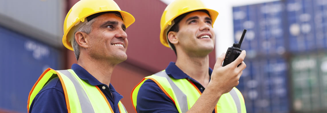 Two men in hard hats and one is holding a handheld radio